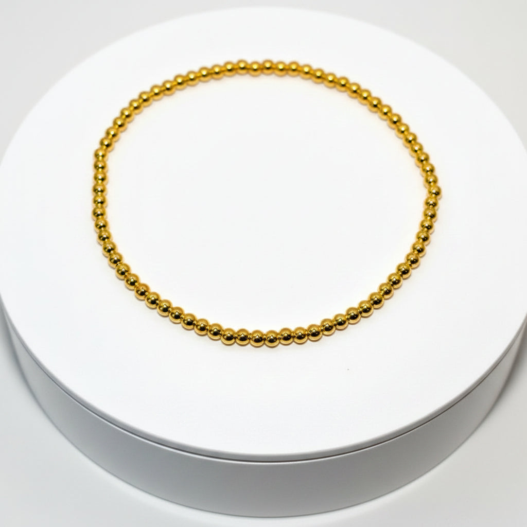 A gold beaded bracelet with a simple design. The bracelet is on a white surface. Design Name: Golden Glaze