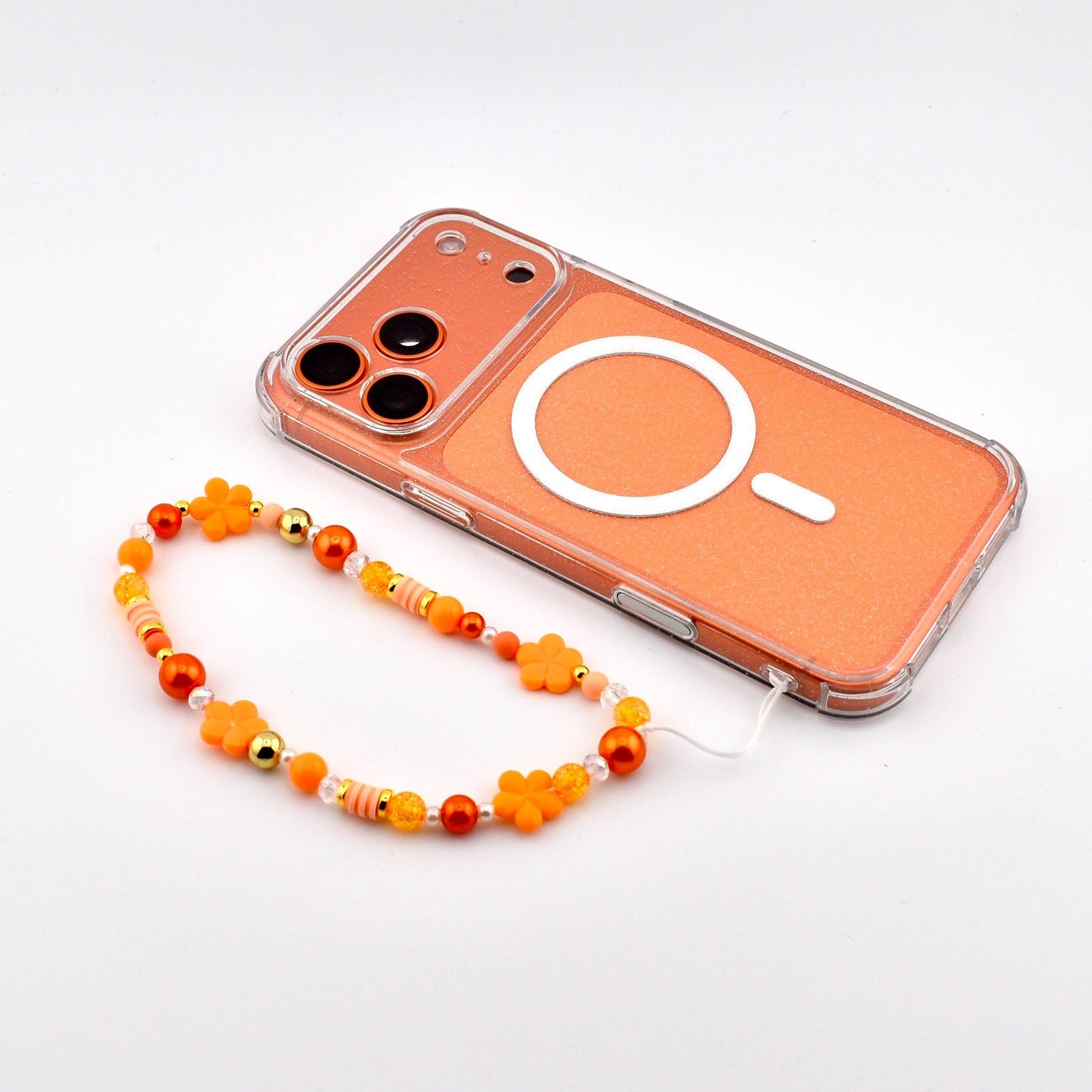 An orange phone with a white circular design and a beaded wrist strap. The strap features orange flower beads, gold beads, and other orange and yellow beads. The phone is clear with an orange backing.
