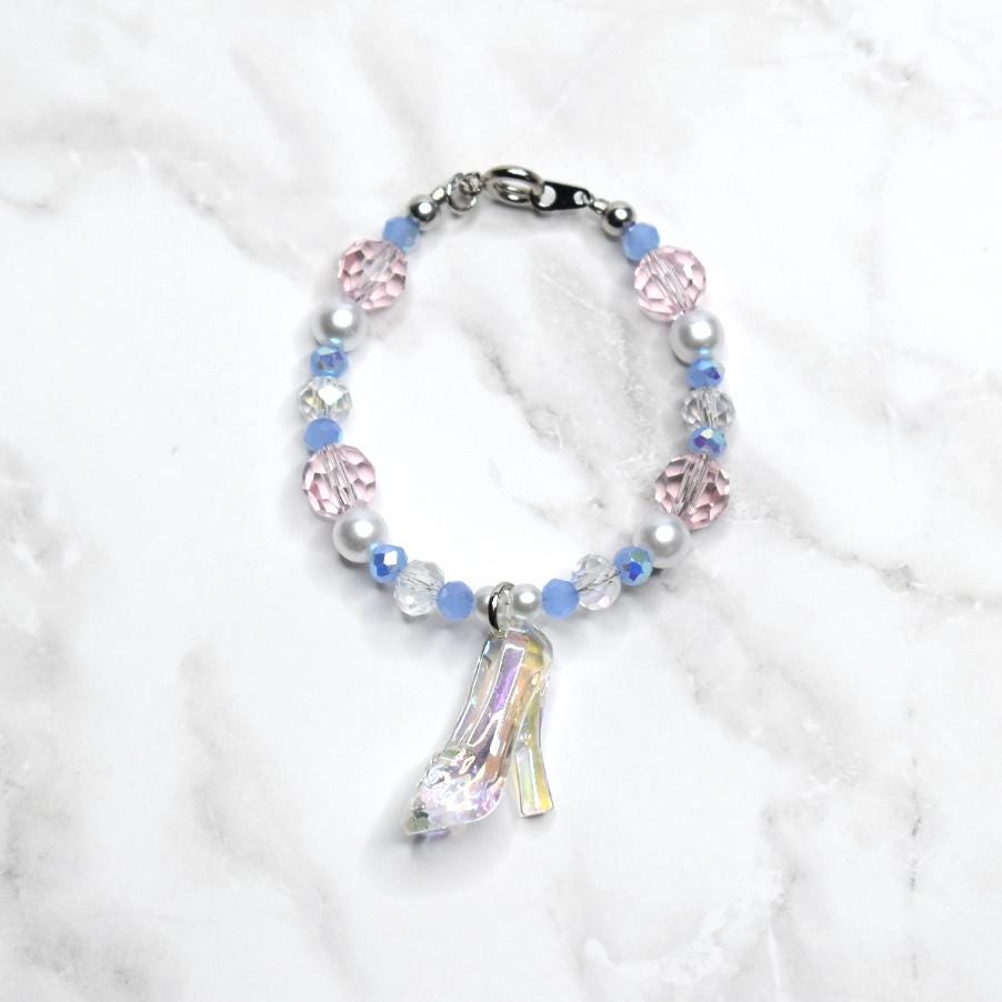 Bracelet with pastel-colored beads and a glass slipper charm on a white marble background