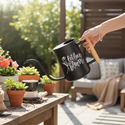 Person watering plants with a black watering can on a patio that says let love bloom