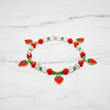 A red and green beaded bracelet with strawberry charms. The bracelet has a white background with the text Design Name: Berry Sweetheart.