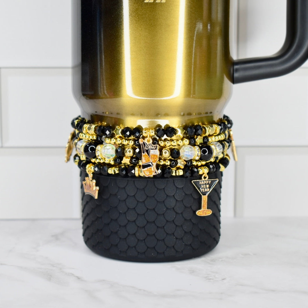 Gold and black honey Stanley with a stack of five new year themed charm bracelets.