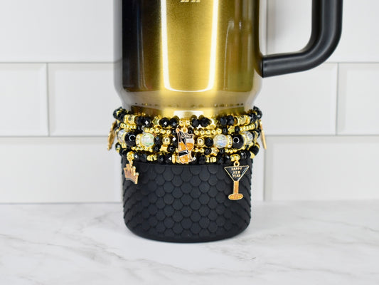 Gold and black honey Stanley with a stack of five new year themed charm bracelets.