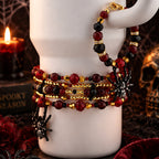 A set of five beaded stretch bracelets with red, black, and gold beads, spider charms, and a black spiderweb clasp, displayed on a white ceramic mug with a gothic Halloween background.