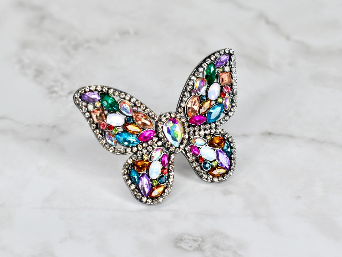 Butterfly-shaped straw charm with multicolored gemstones on a marble background