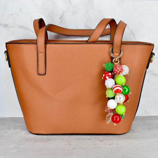 Brown handbag with a colorful Christmas bead charm on a light gray surface.