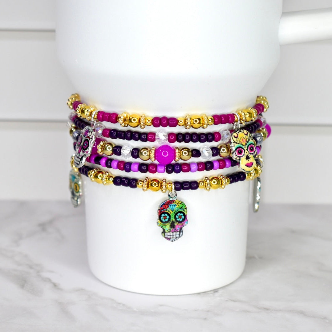 Colorful beaded bracelets with skull charms on a white mug against a marble background