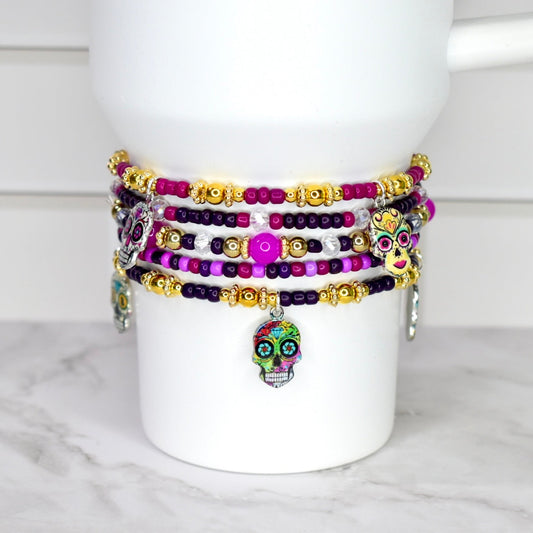 Colorful beaded bracelets with skull charms on a white mug against a marble background