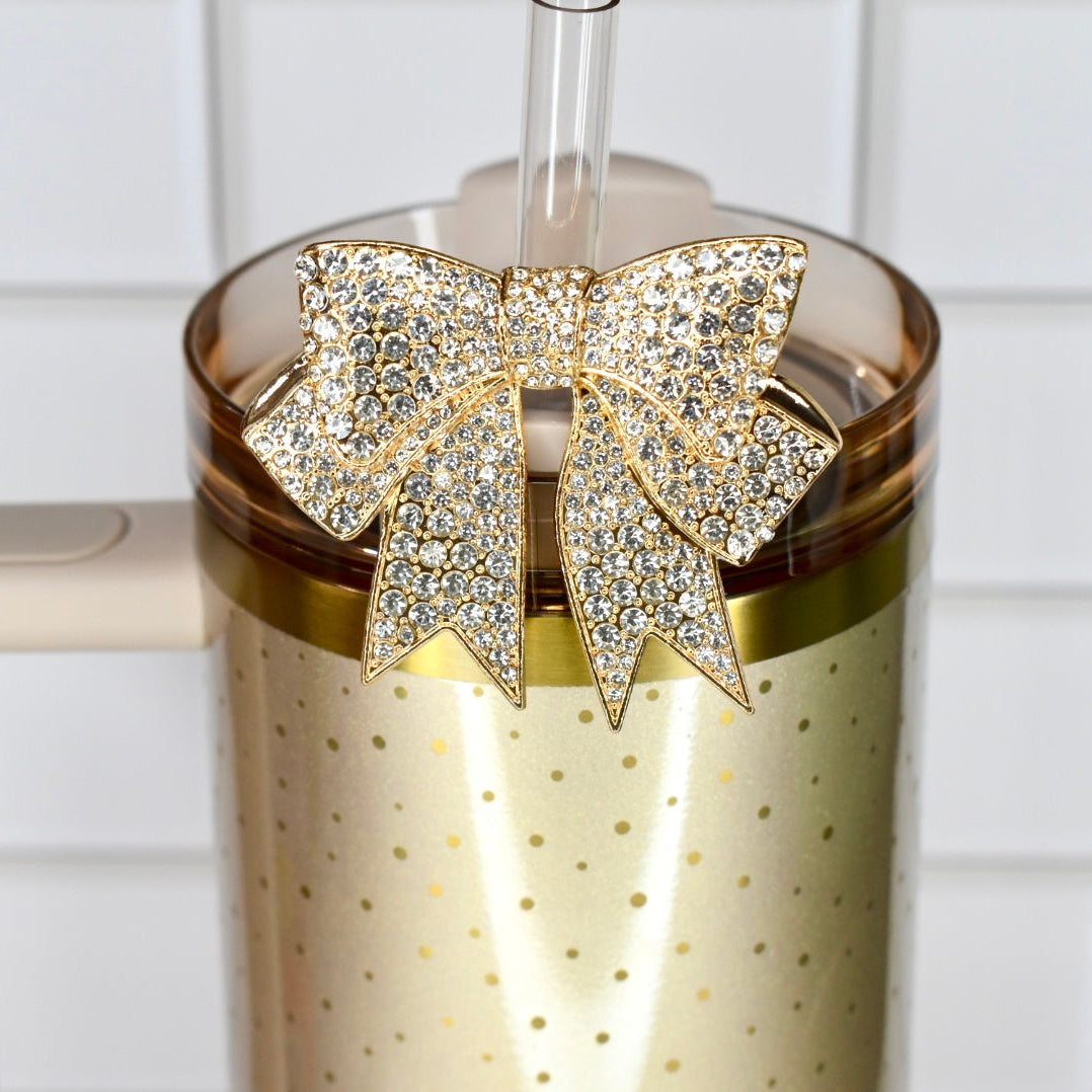 Gold tumbler with a decorative bow on a white tiled background