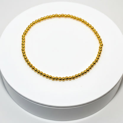 A gold beaded bracelet with a simple design. The bracelet is on a white surface. Design Name: Golden Glaze