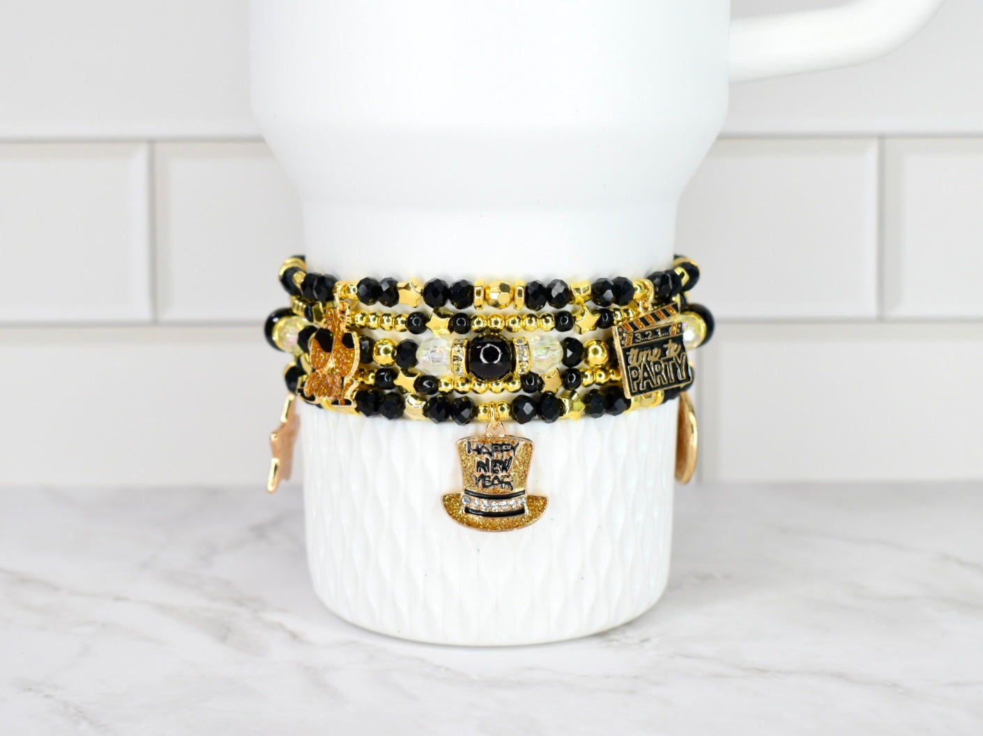 Set of black and gold beaded bracelets on a white Stanley against a white tiled wall background.
