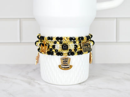 Set of black and gold beaded bracelets on a white Stanley against a white tiled wall background.