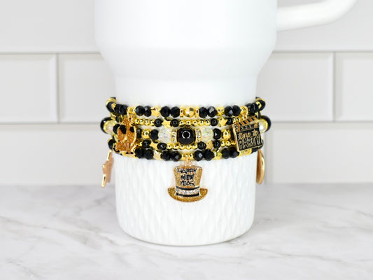 Set of black and gold beaded bracelets on a white Stanley against a white tiled wall background.