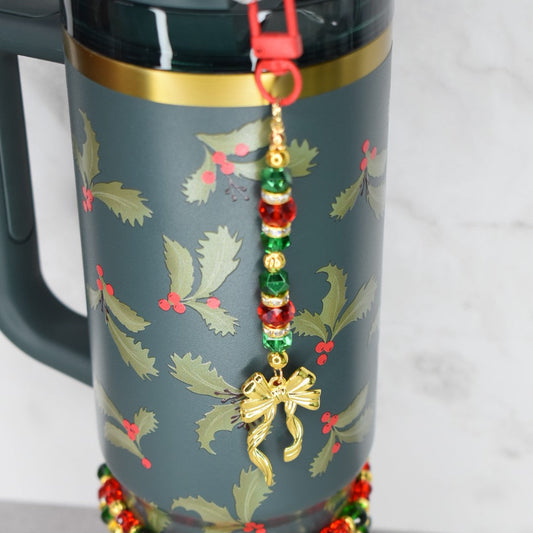 Holiday botanical Stanley tumbler with red green gold straw charm that has a gold bow charm at the bottom