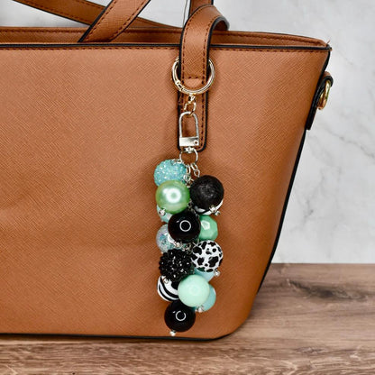 Beaded keychain attached to a brown handbag on a wooden surface with a marble background.