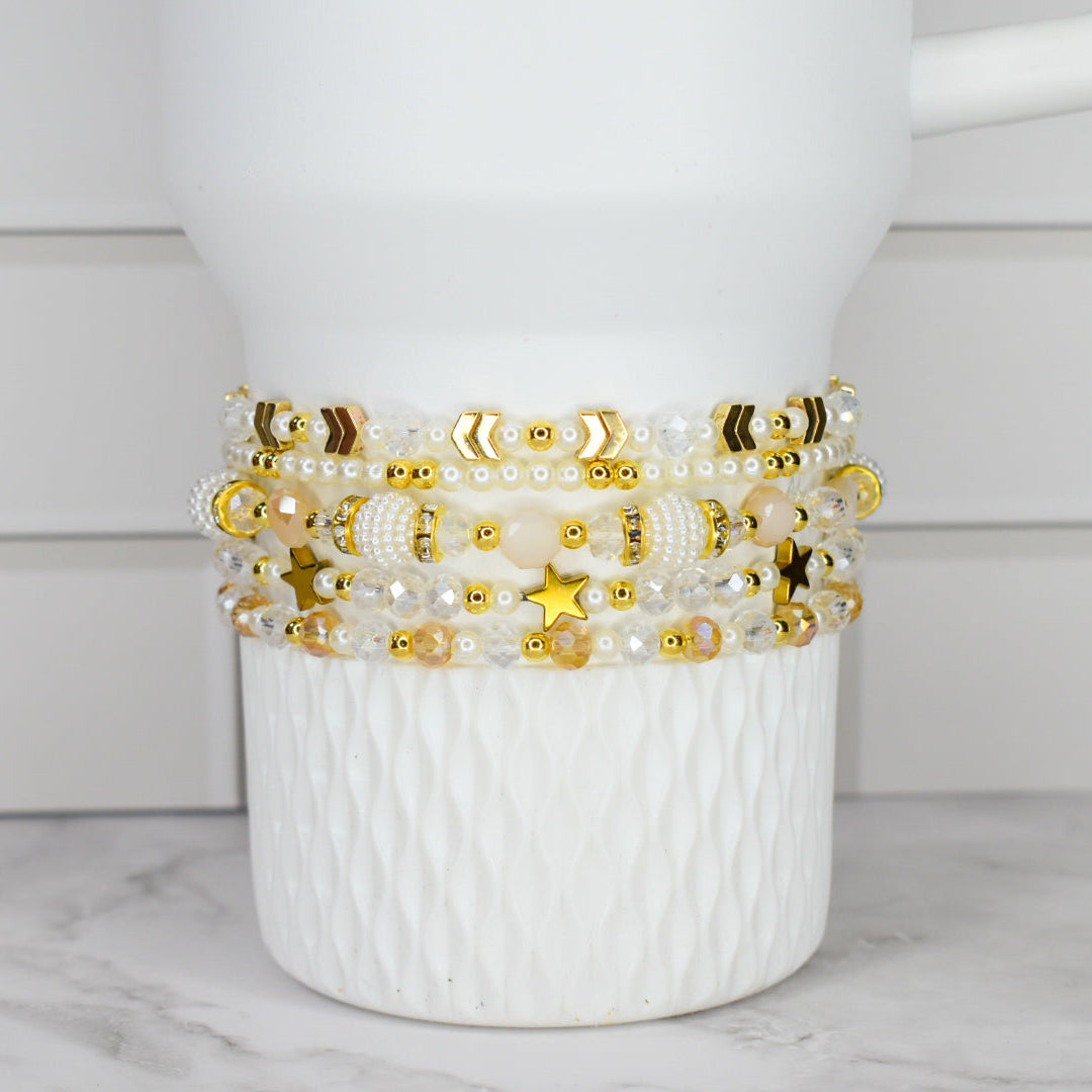 Pearl crystal and gold bracelet stack on a white stanley tumbler.