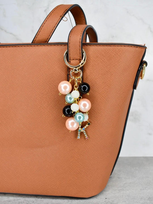 Brown handbag with a decorative keychain featuring colorful beads and a small initial on a light gray background.