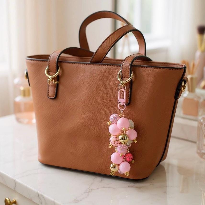Brown handbag with a decorative pink and gold charm on a marble surface.