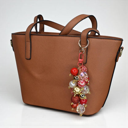 Brown handbag with a colorful red and gold beaded keychain on a white background