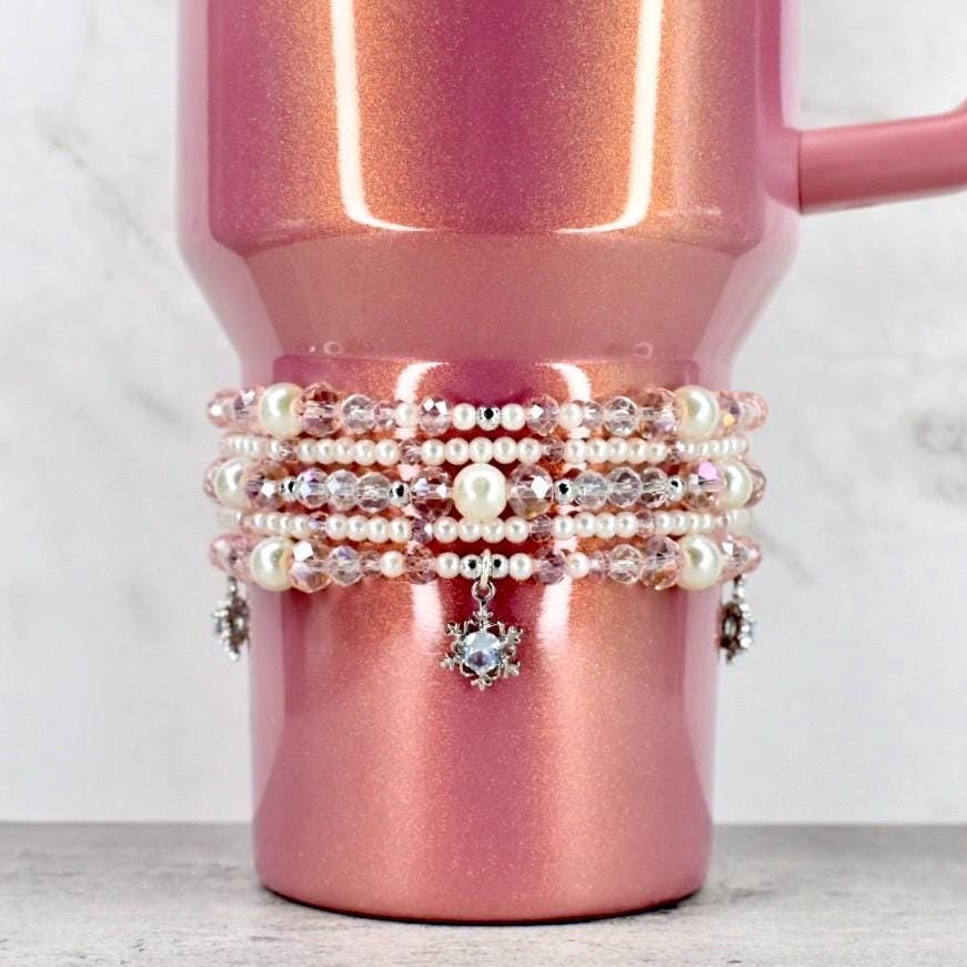 Pink glittery mug with multiple pearl bracelets on a white background