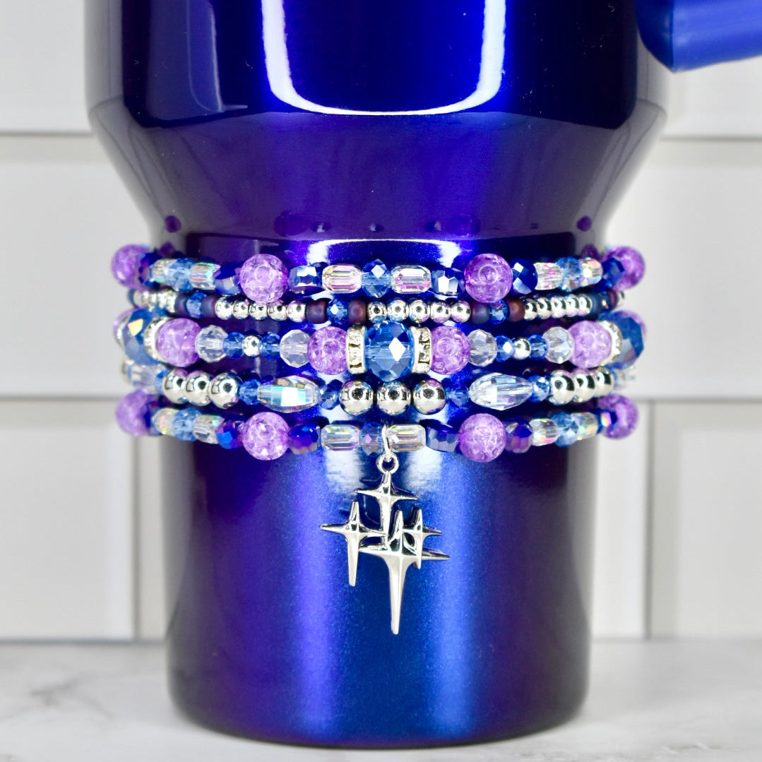 Blue mug with multiple beaded bracelets stacked on top, against a white tiled wall background.