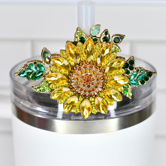 Decorative rhinestone sunflower straw charm on a white Stanley tumbler with a tile background.
