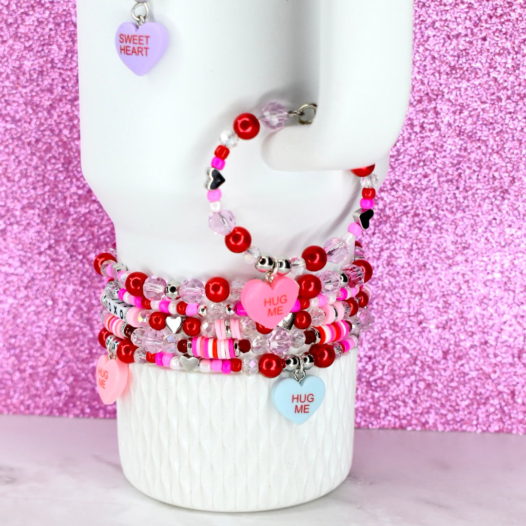 Stack of colorful beaded bracelets on a mannequin arm against a pink glittery background