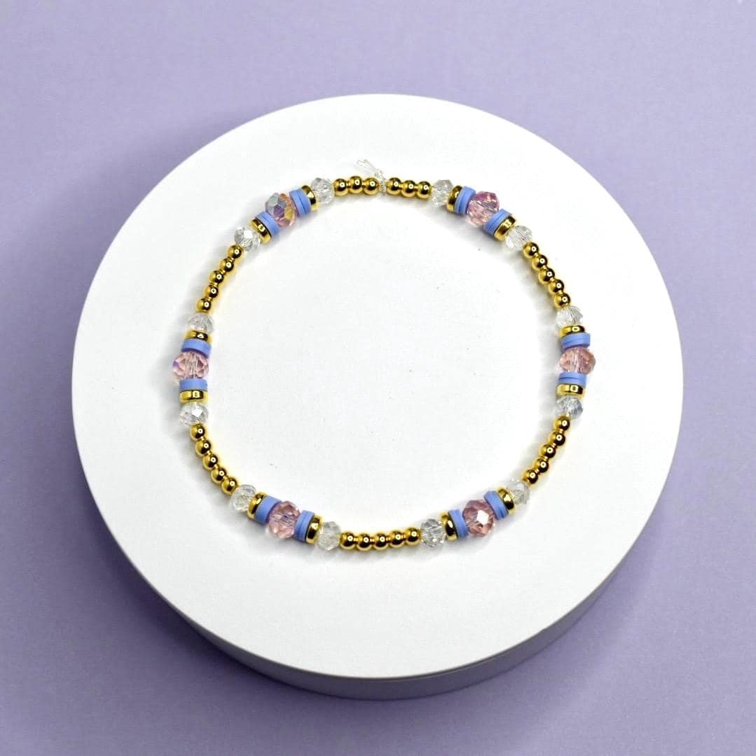Bracelet with gold and multicolored beads on a white stand against a purple background