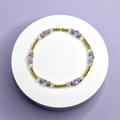 Bracelet with gold and multicolored beads on a white stand against a purple background