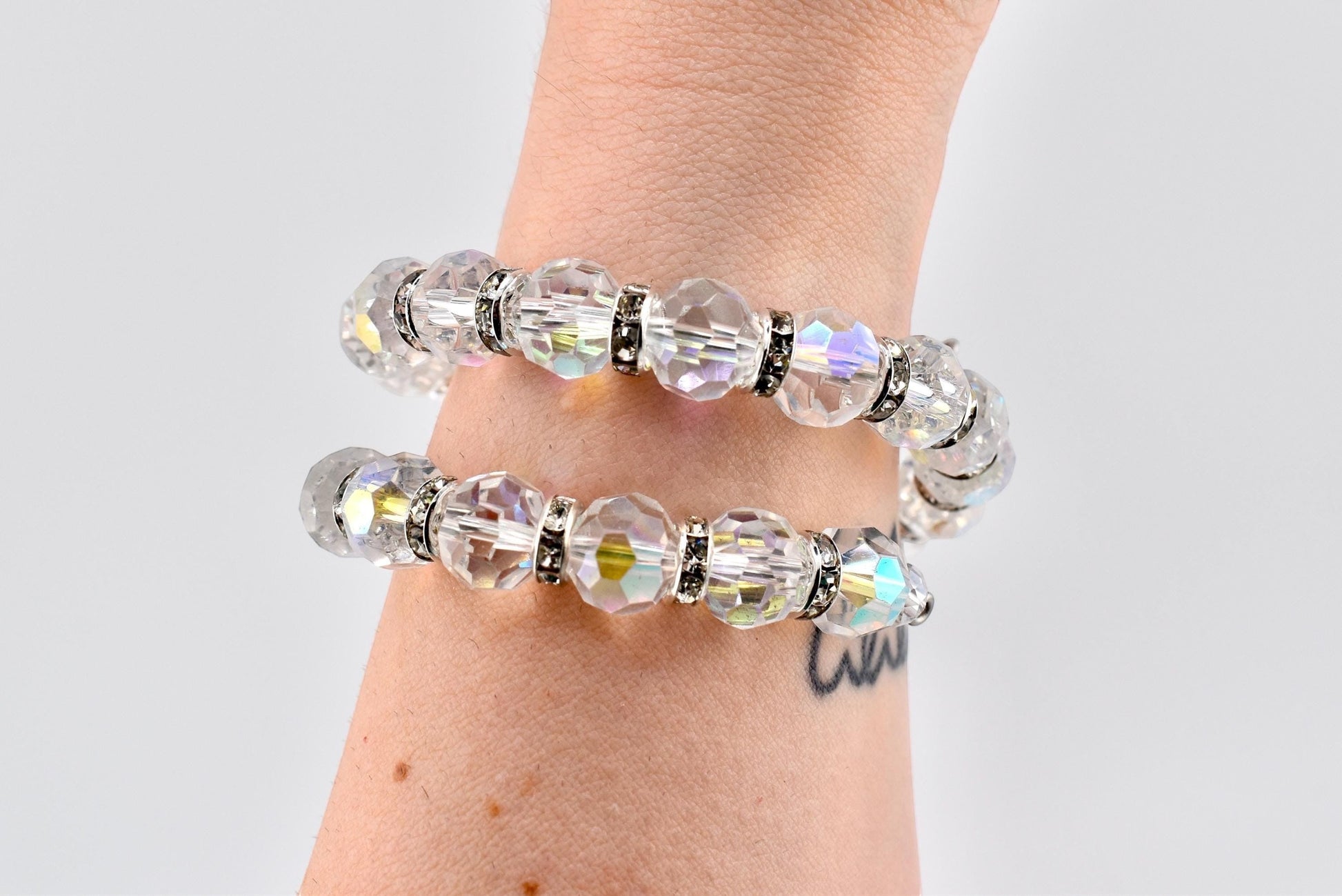 Calathea Collective iridescent crystal wrap bracelet with rhinestone spacer beads on a wrist. The bracelet has a subtle pink, blue, and gold shimmer.