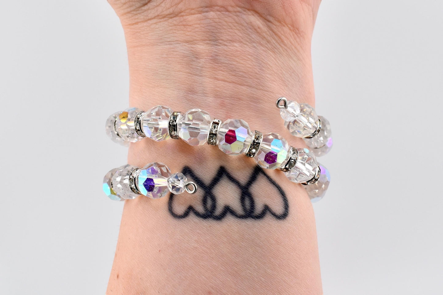 Calathea Collective iridescent crystal wrap bracelet with rhinestone spacers on wrist. Features faceted AB finish crystals and silver-tone spacers.