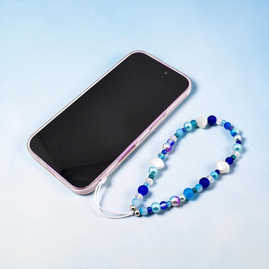 Calathea Collective ocean blue seashell phone charm wrist strap with pearl and glass beads. Features silver-tone seashell charms and a blue, aqua, and purple color palette.