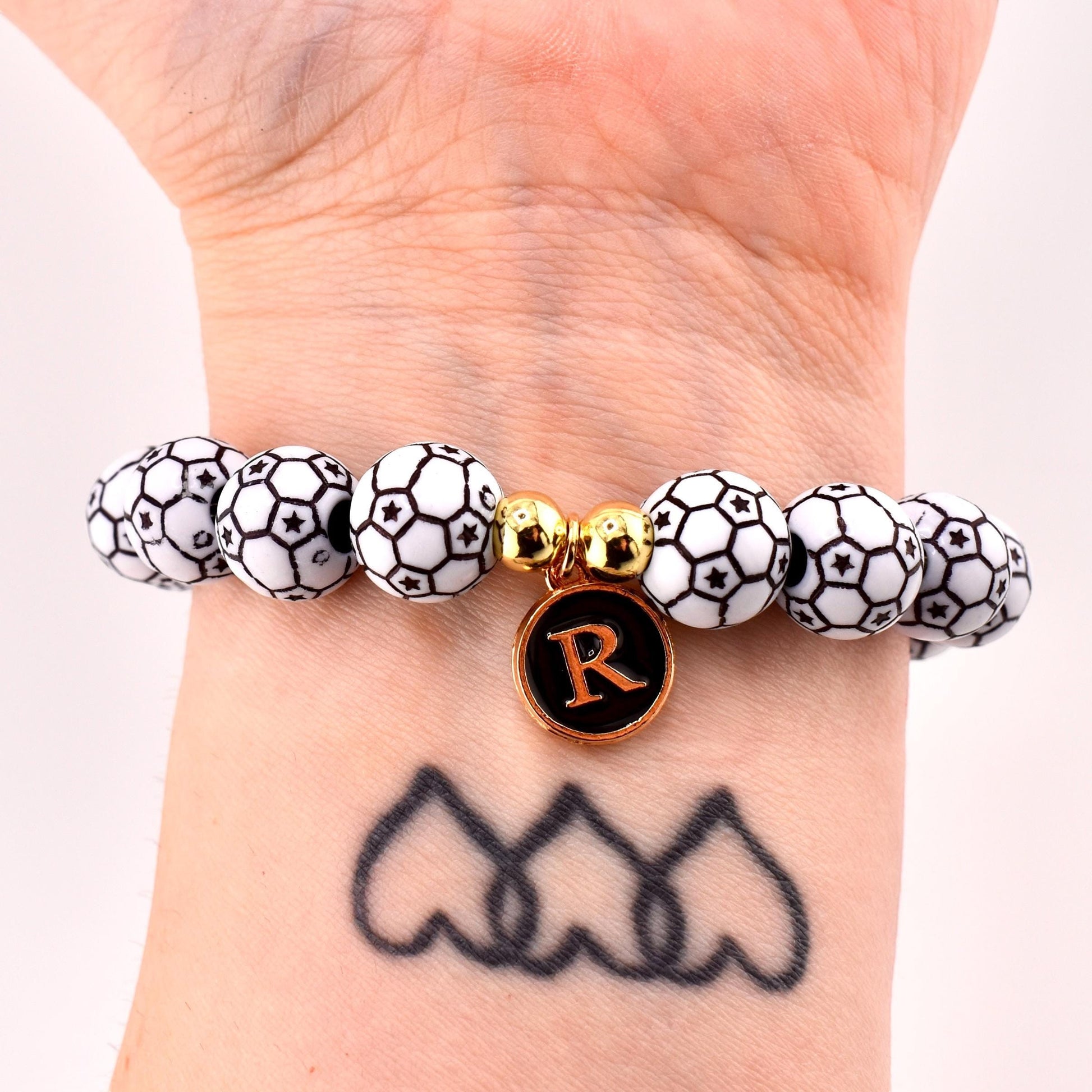 Calathea Collective soccer ball beaded bracelet with letter R charm and gold accent beads on a wrist.
