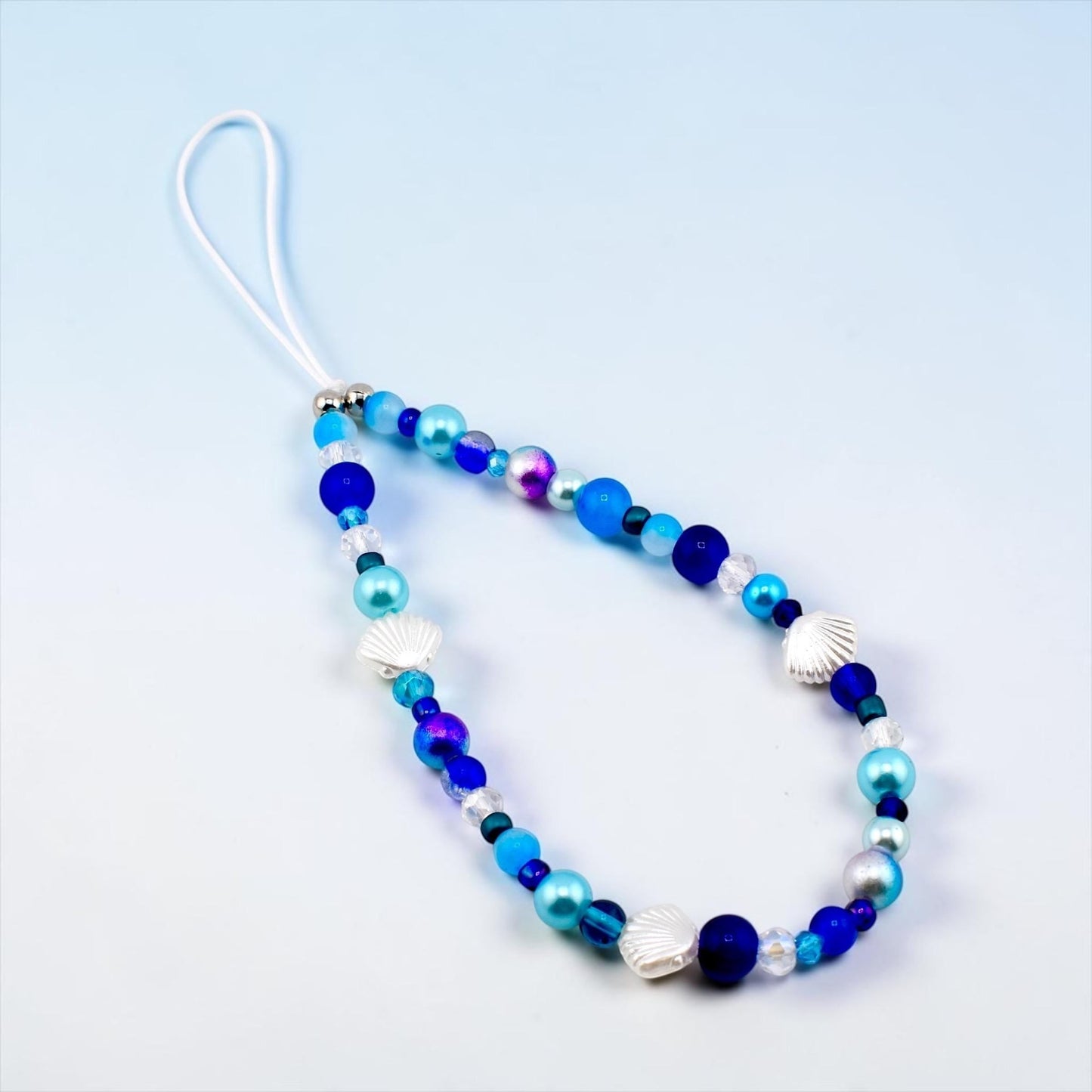 Calathea Collective ocean blue seashell phone charm wrist strap with pearl and glass beads, silver-tone seashell accents.