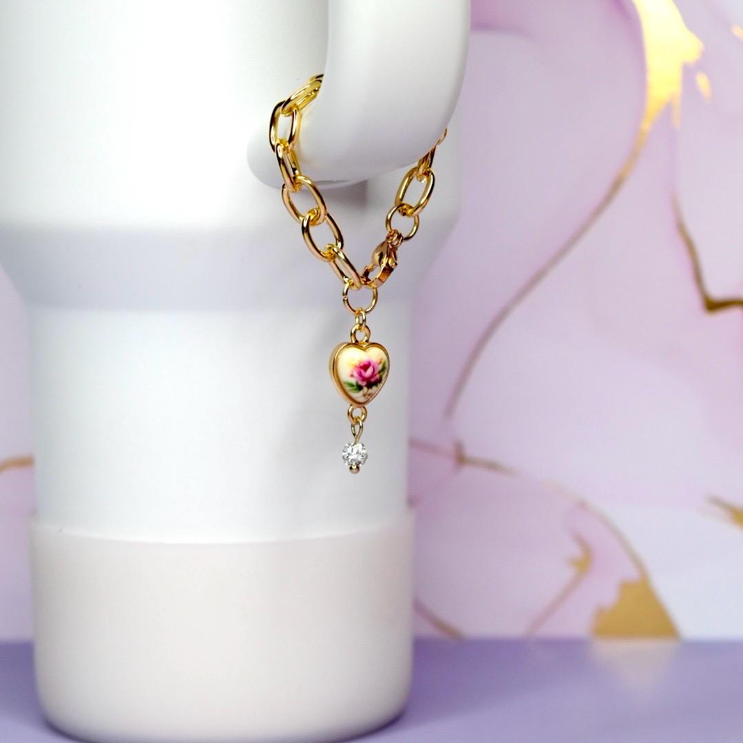 Gold chain necklace with a heart-shaped pendant on a white tumbler against a floral background