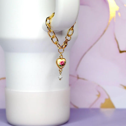 Gold chain necklace with a heart-shaped pendant on a white tumbler against a floral background