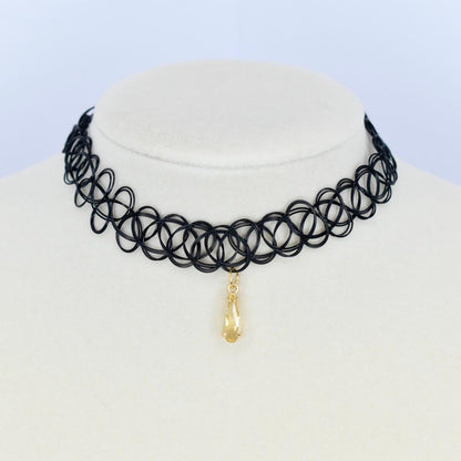 Black choker necklace with a gold pendant on a mannequin head against a light blue background