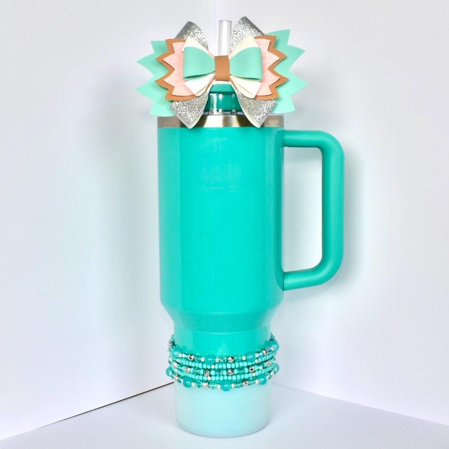 Turquoise mug with decorative bow and beads on a white background