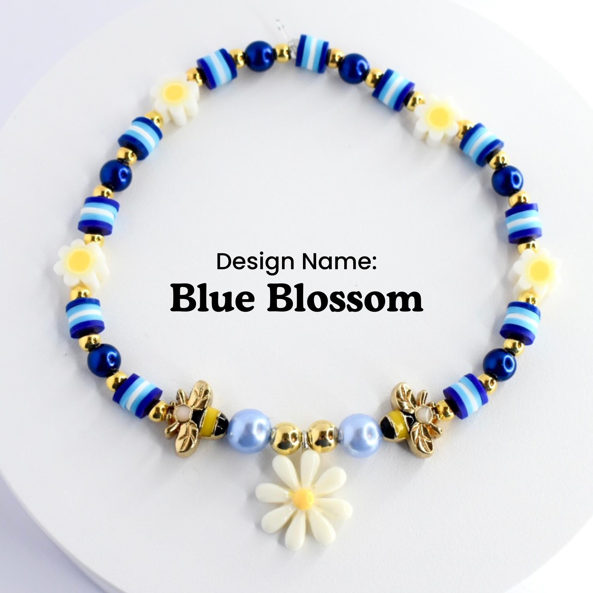 A blue and white beaded bracelet with a gold bee charm and a white daisy charm. The bracelet has a blue and white striped pattern and is decorated with small white flowers. The text 'Design Name: Blue Blossom' is printed below the bracelet.