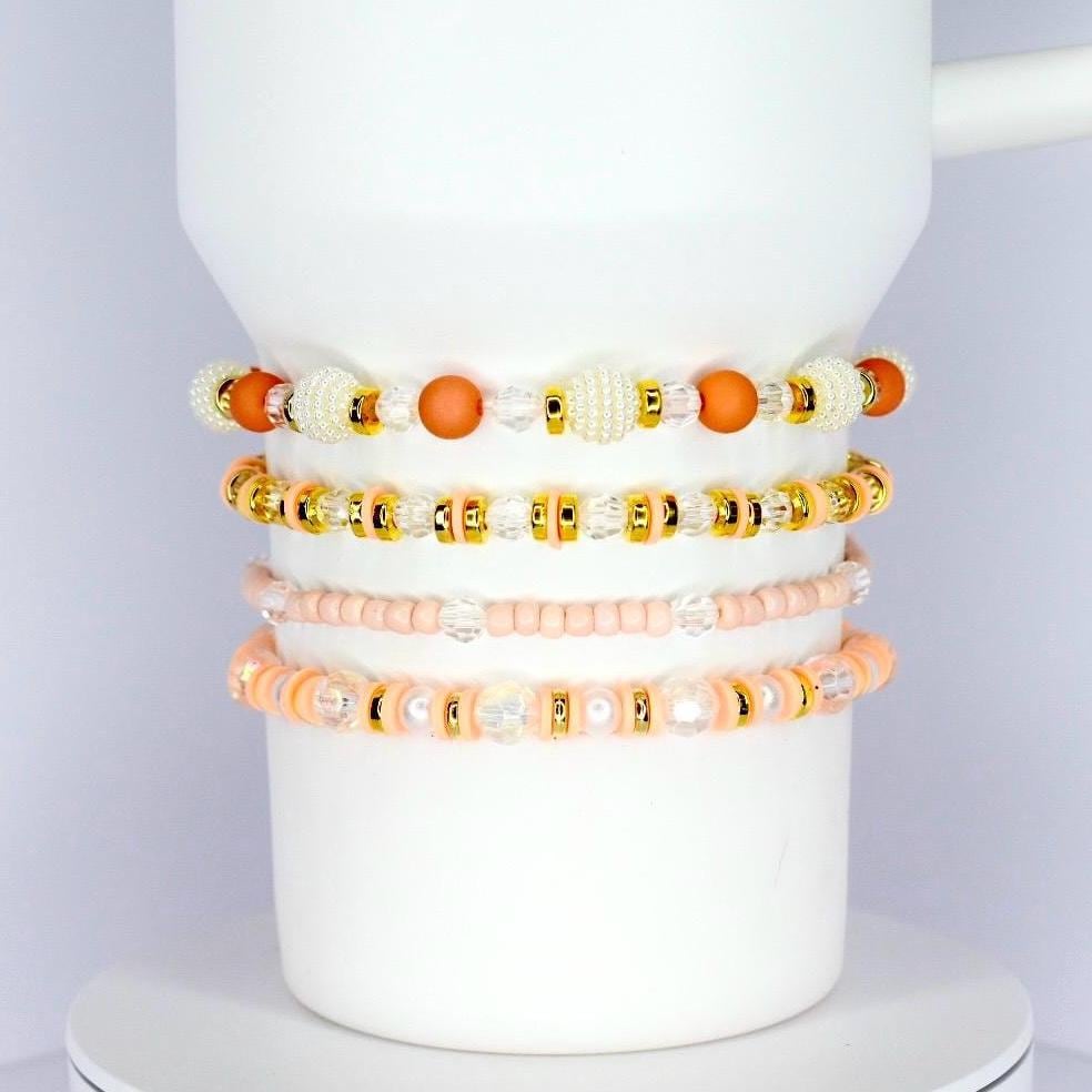 Handmade tumbler bracelet set with peach, pearl, and gold beads, stacked around a white tumbler for a soft and elegant look.