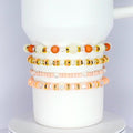 Handmade tumbler bracelet set with peach, pearl, and gold beads, stacked around a white tumbler for a soft and elegant look.