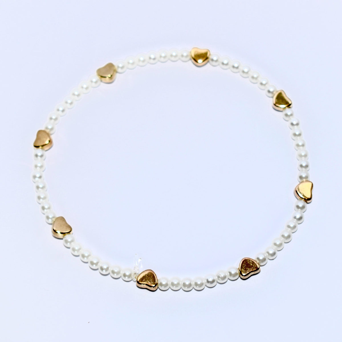 A white pearl bracelet with gold heart charms. The bracelet is made of small, white pearls and has seven gold heart charms evenly spaced around the bracelet.