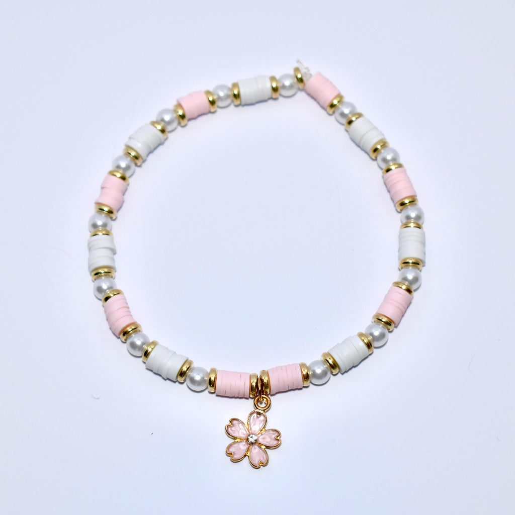 A white and pink beaded bracelet with a gold charm in the shape of a pink flower with a rhinestone center.
