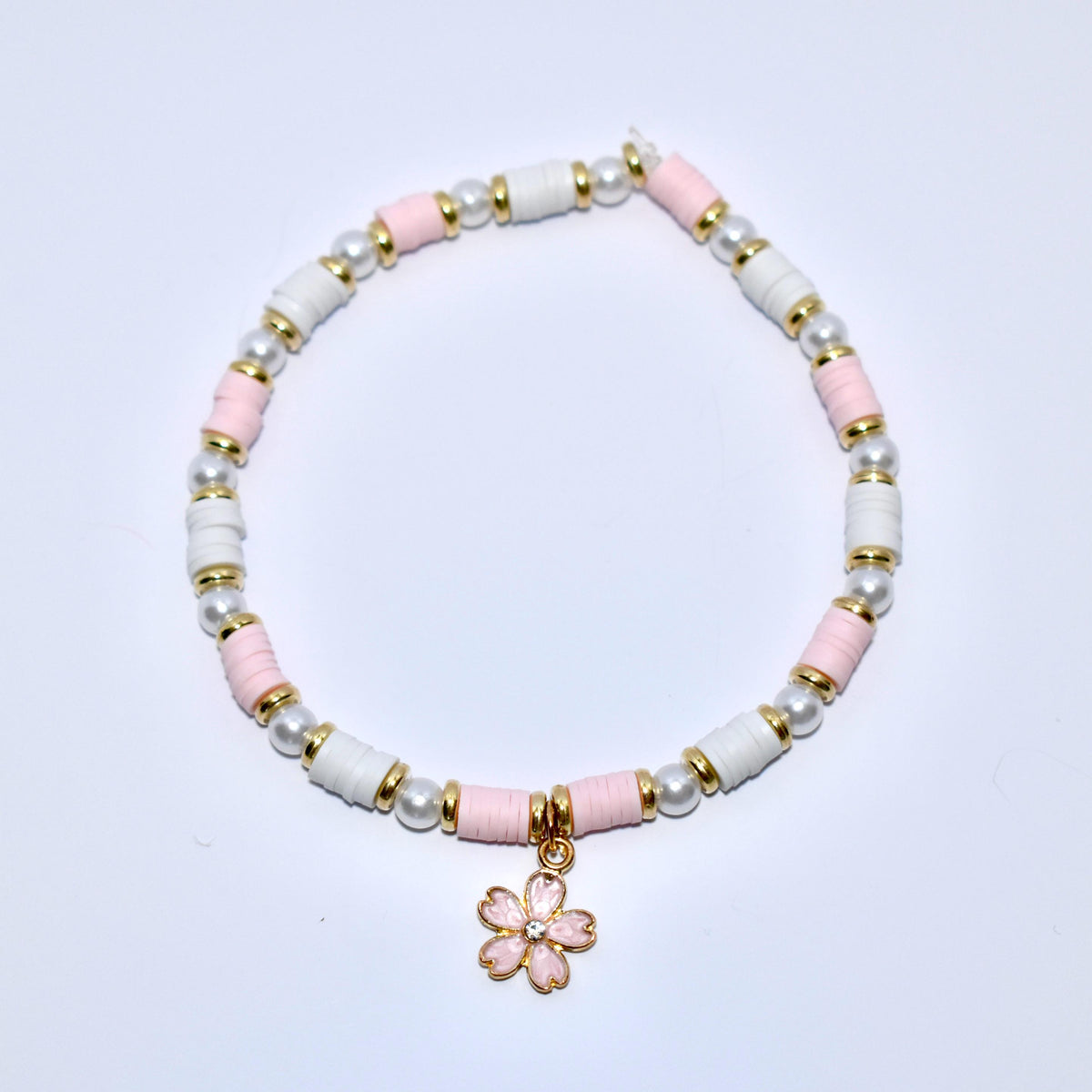 A white and pink beaded bracelet with a gold charm in the shape of a pink flower with a rhinestone center.