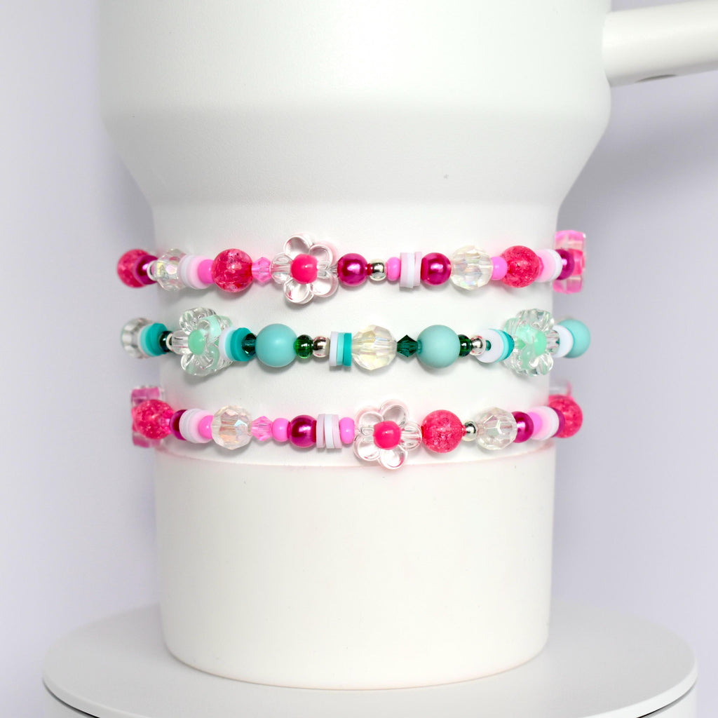 Three pink, white, and turquoise beaded bracelets with flower charms. The bracelets are stacked on top of each other.
