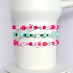Three pink, white, and turquoise beaded bracelets with flower charms. The bracelets are stacked on top of each other.
