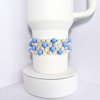 A white Stanley with a blue and white beaded wrap. The beads are alternating colors and are made of a smooth material.