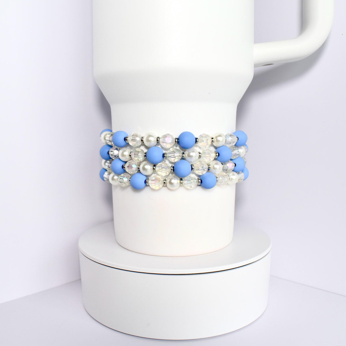A white Stanley with a blue and white beaded wrap. The beads are alternating colors and are made of a smooth material.