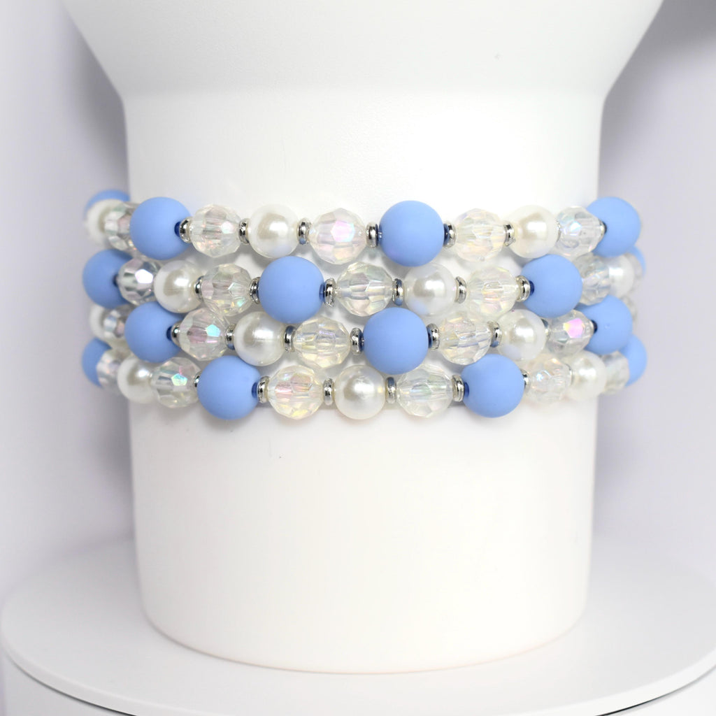 Four bracelets made of light blue and white beads. The bracelets feature alternating light blue matte beads and clear iridescent beads. The bracelet also includes white pearl beads.