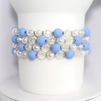 Four bracelets made of light blue and white beads. The bracelets feature alternating light blue matte beads and clear iridescent beads. The bracelet also includes white pearl beads.